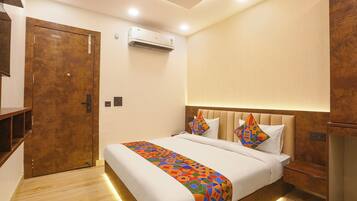 A hotel room with a bed, a wooden wardrobe, an air conditioning unit, and a wall-mounted light fixture.