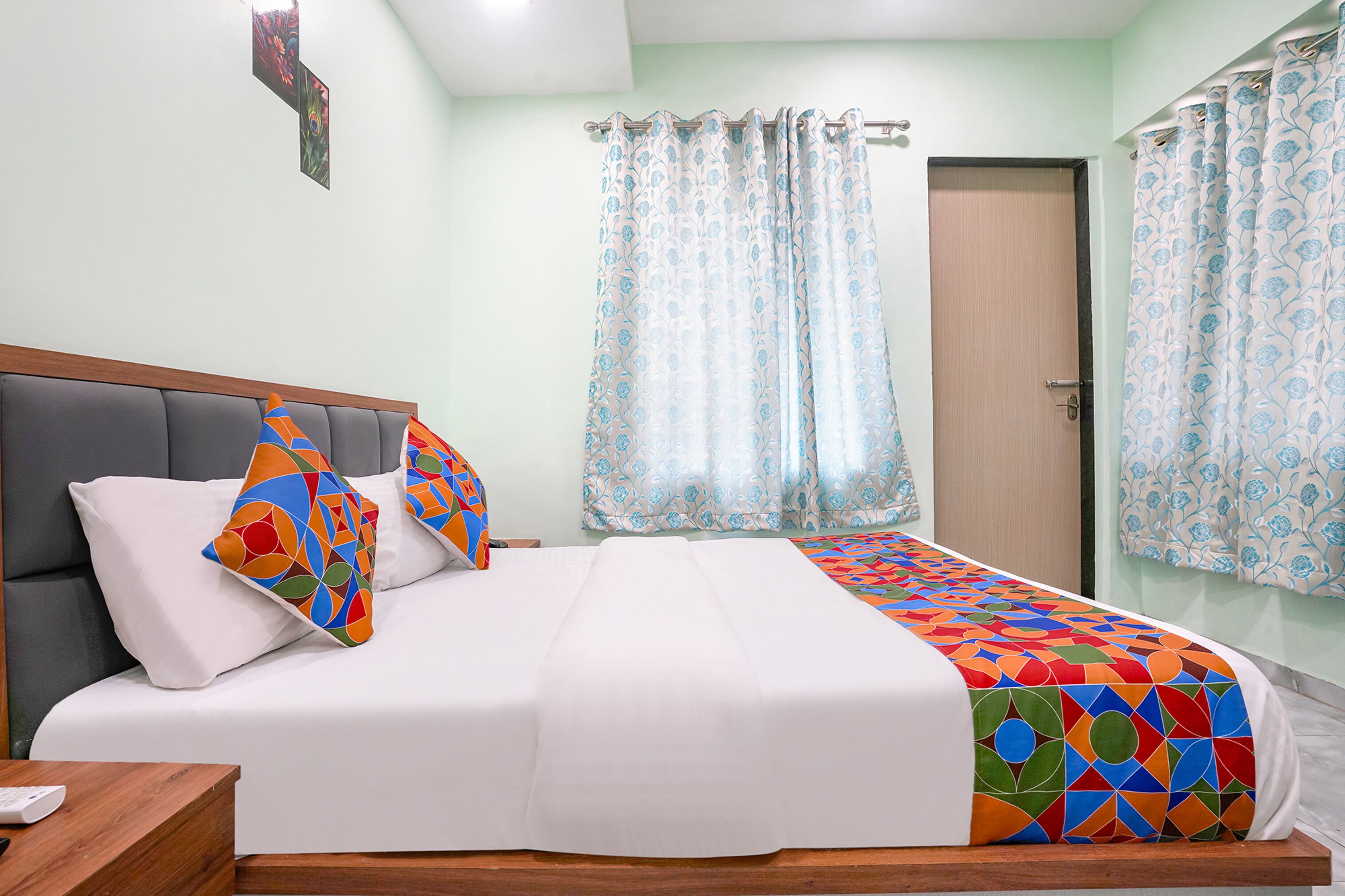Un lit bien fait, recouvert d’une couverture aux motifs géométriques colorés, avec une tête de lit rembourrée grise et deux coussins aux motifs géométriques multicolores.