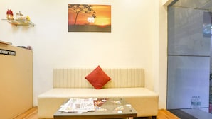 A reception area with a sofa, a glass coffee table with newspapers, a red pillow, a wall-mounted shelf with items, and a sunset painting. - Via 24/7 (Navi Mumbai)