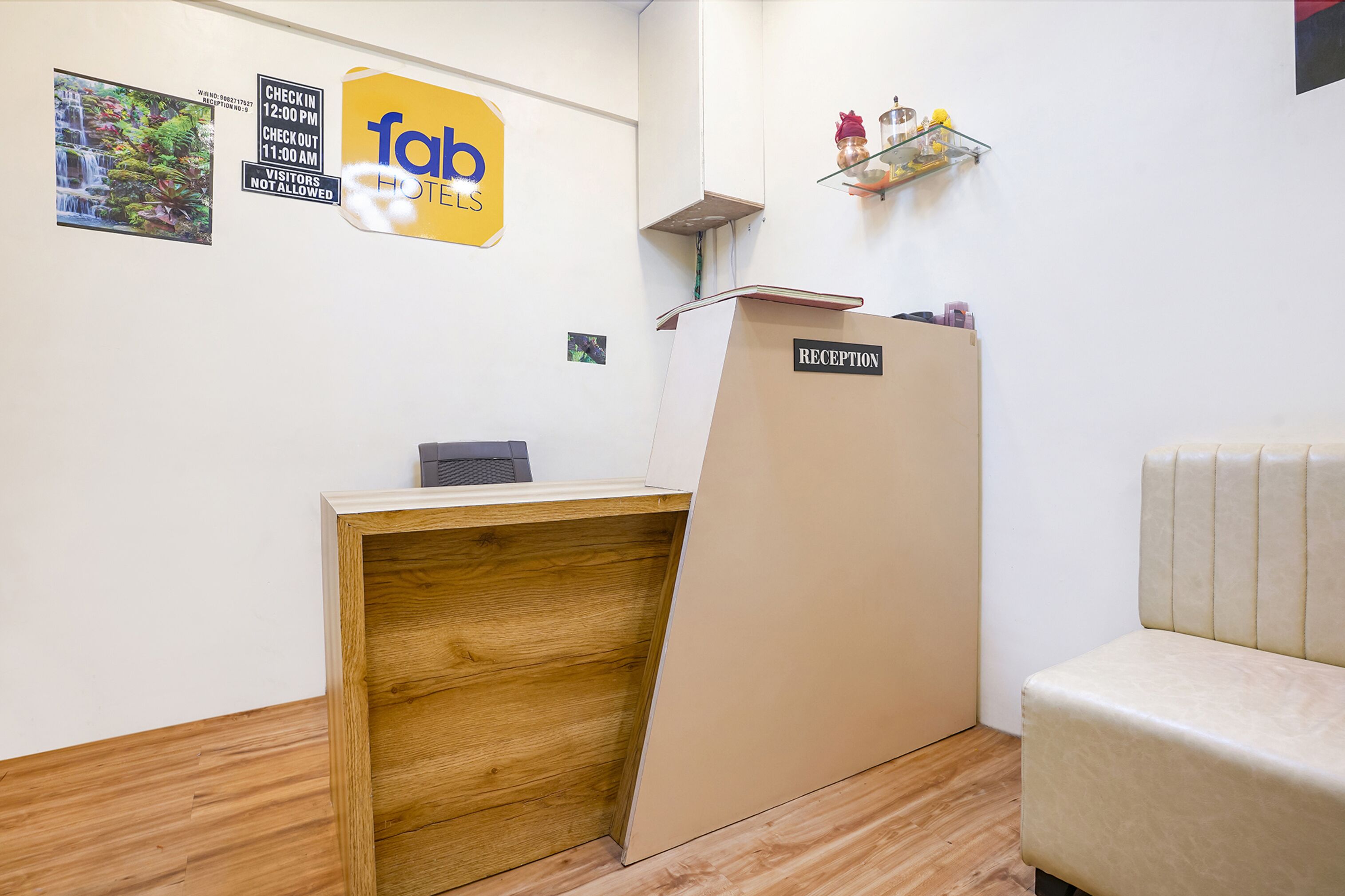 A reception desk with a wooden counter and a beige reception area. There is a reception sign on the wall and a small shelf with decorative items.