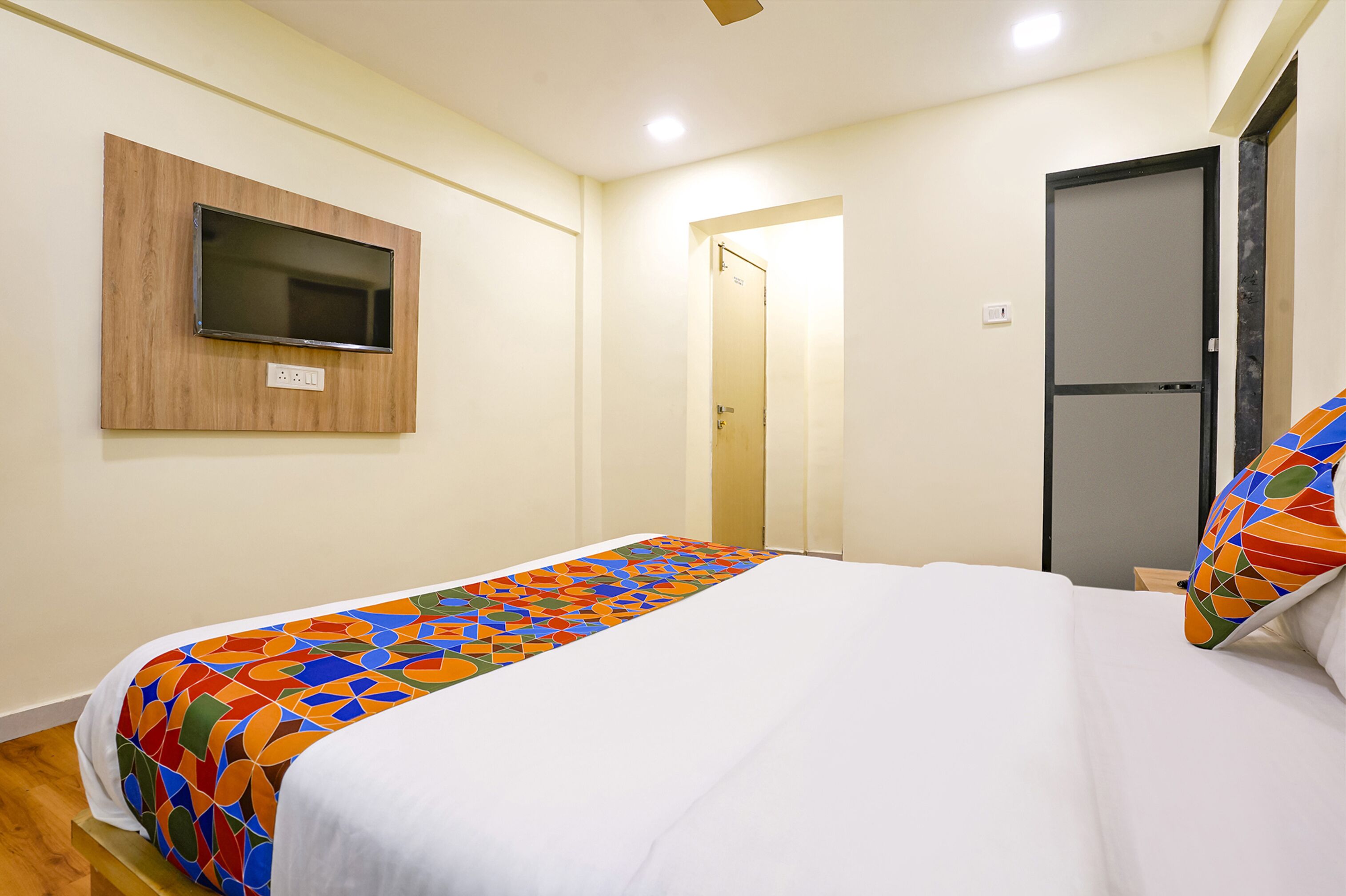 Habitación de hotel con cama, televisor montado en la pared y puerta que da a otra habitación.