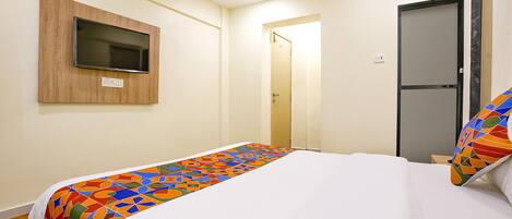 Habitación de hotel con cama, televisor montado en la pared y puerta que da a otra habitación.