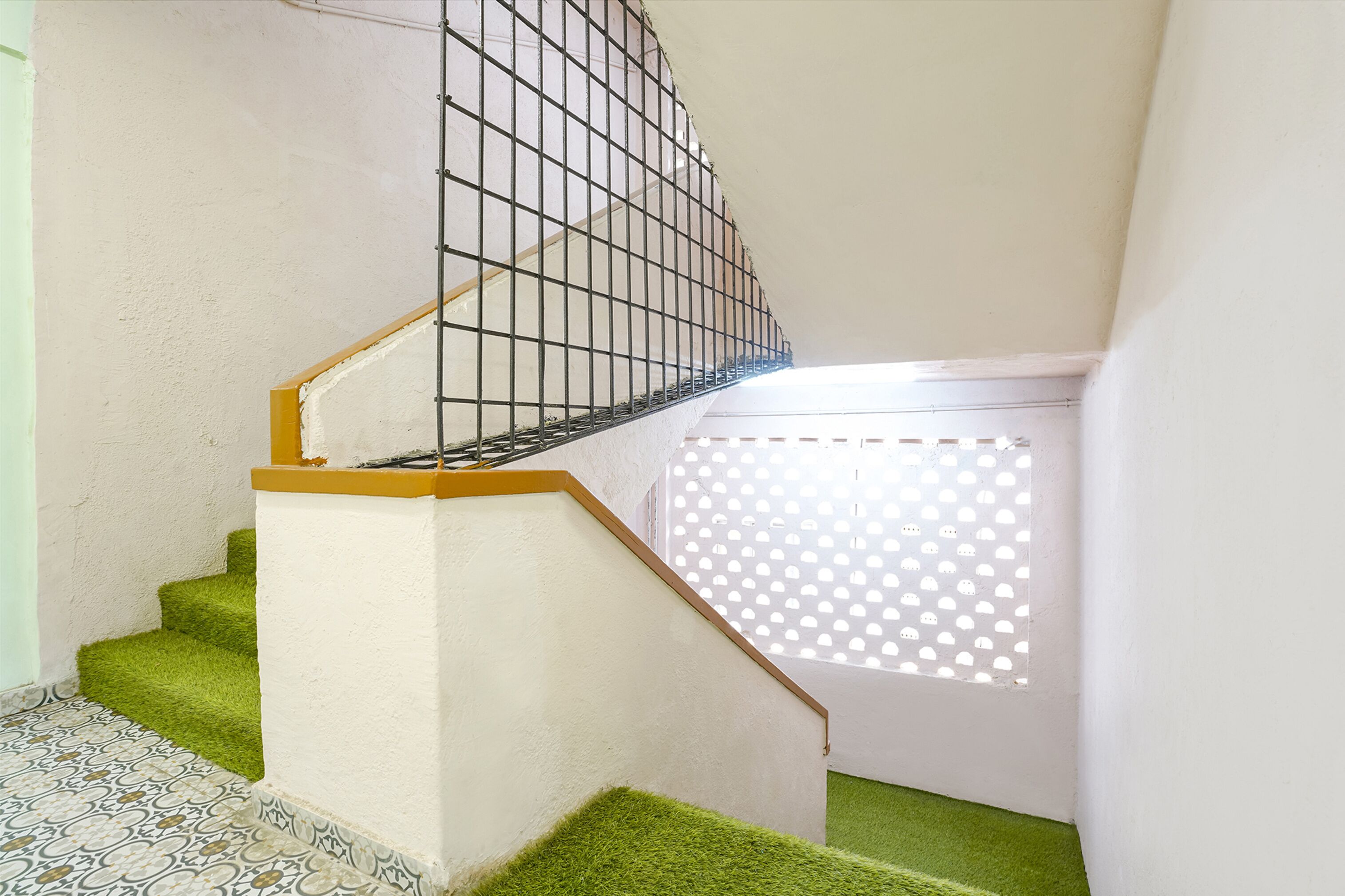 Eine Treppe mit grünen Teppichstufen, einem Holzgeländer und einem Metallschutzgitter.