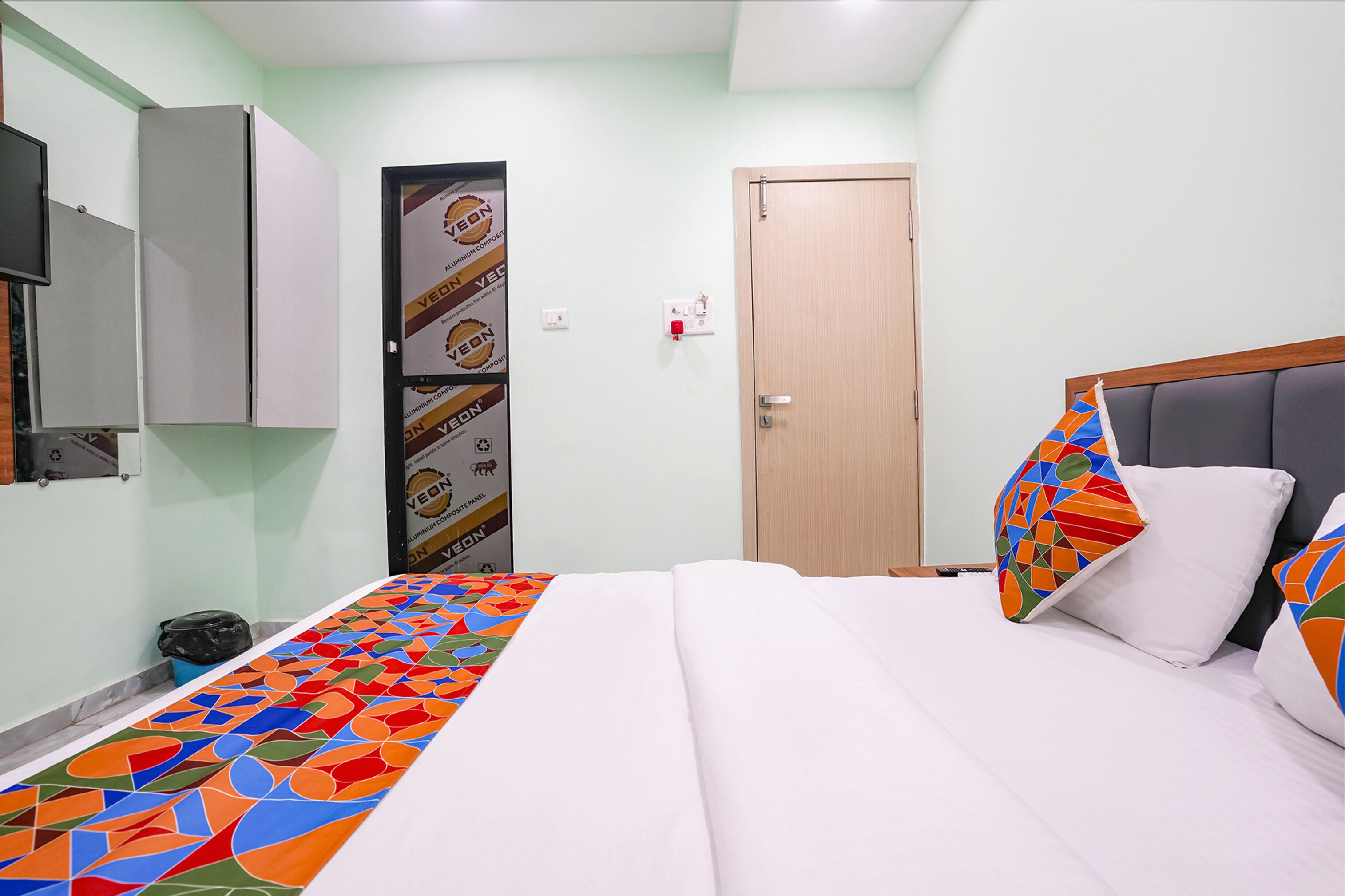 Habitación de hotel con cama, puerta de madera, televisor montado en la pared y cubrecama estampado.