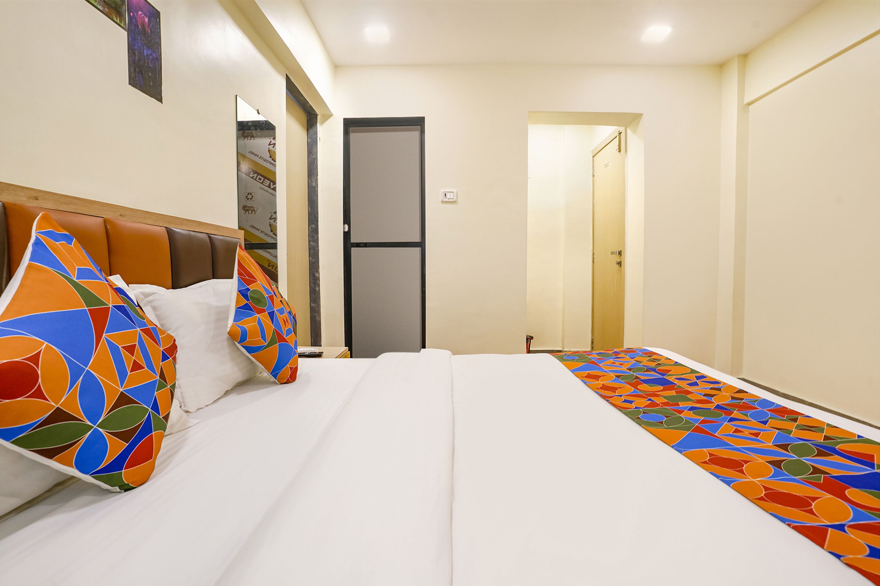 Une chambre d’hôtel avec un lit, des oreillers, une porte et un mur orné d’une affiche.