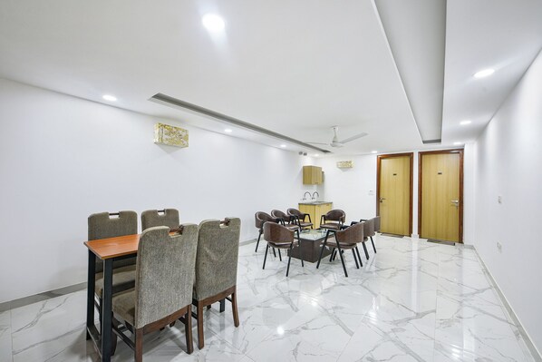 A conference room with a marble floor, grey upholstered chairs, a wooden table, a ceiling fan, and wooden doors. - FabHotel Luxe 8 Stayz - Phase 1 Metro, Golf Course Road (Gurugram)