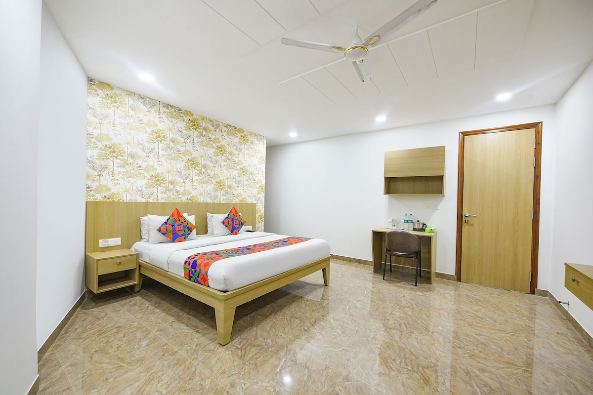 Habitación de hotel con cama, escritorio, silla, armario, ventilador de techo y pared con papel tapiz floral.