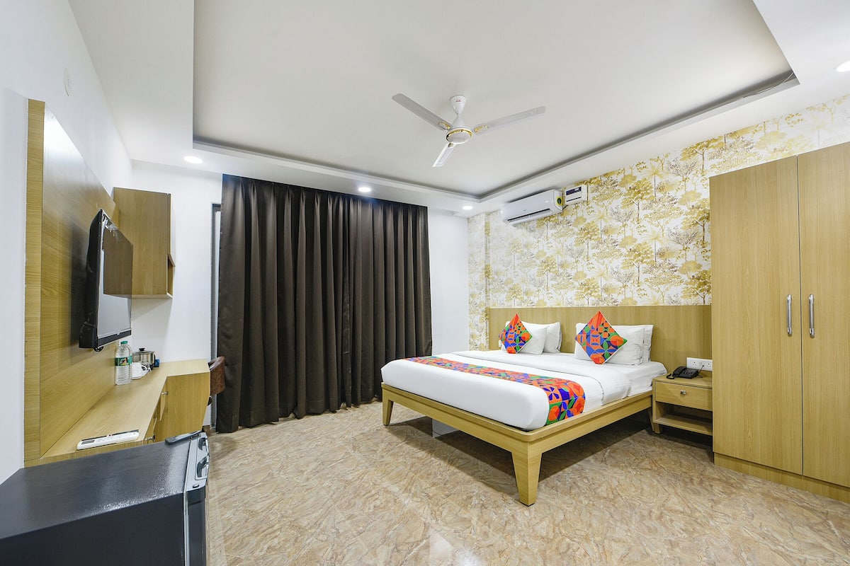 Habitación de hotel con cama, armario, escritorio con computadora, espejo y ventilador de techo.