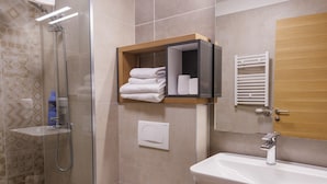 Une salle de bain moderne avec une douche à parois de verre, des toilettes blanches, un lavabo avec un meuble-vasque en bois et un porte-serviettes.