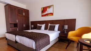 Une chambre d’hôtel avec un grand lit, une armoire en bois, des tables de chevet et un fauteuil jaune.