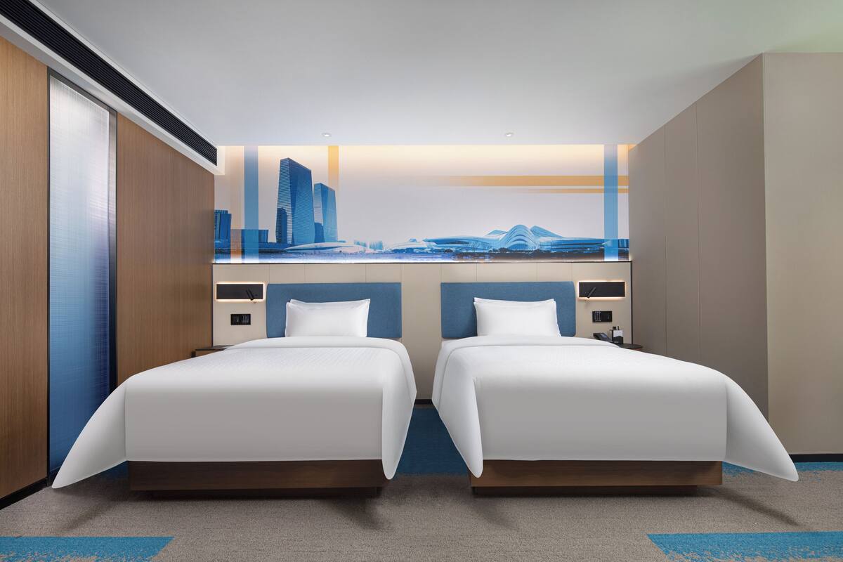 A hotel room with two beds, a cityscape mural on the wall, and a modern design.