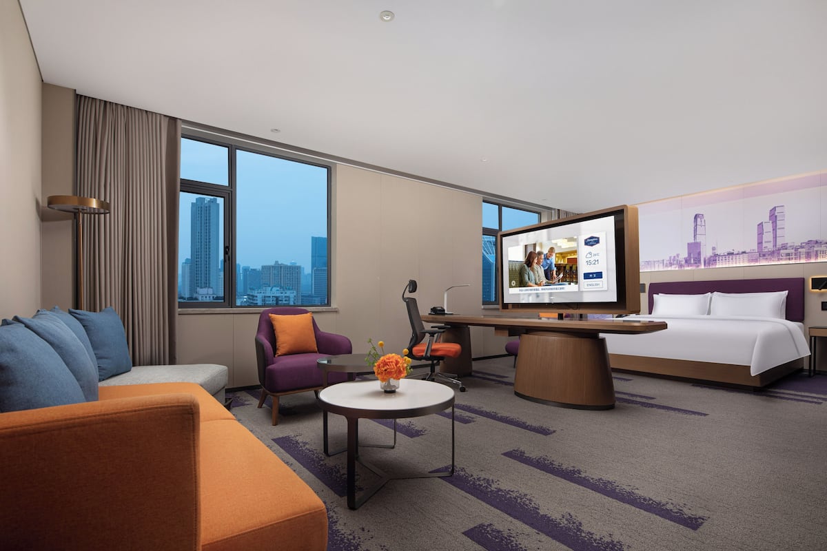 A hotel room with a bed, a sofa, a desk, and a TV.