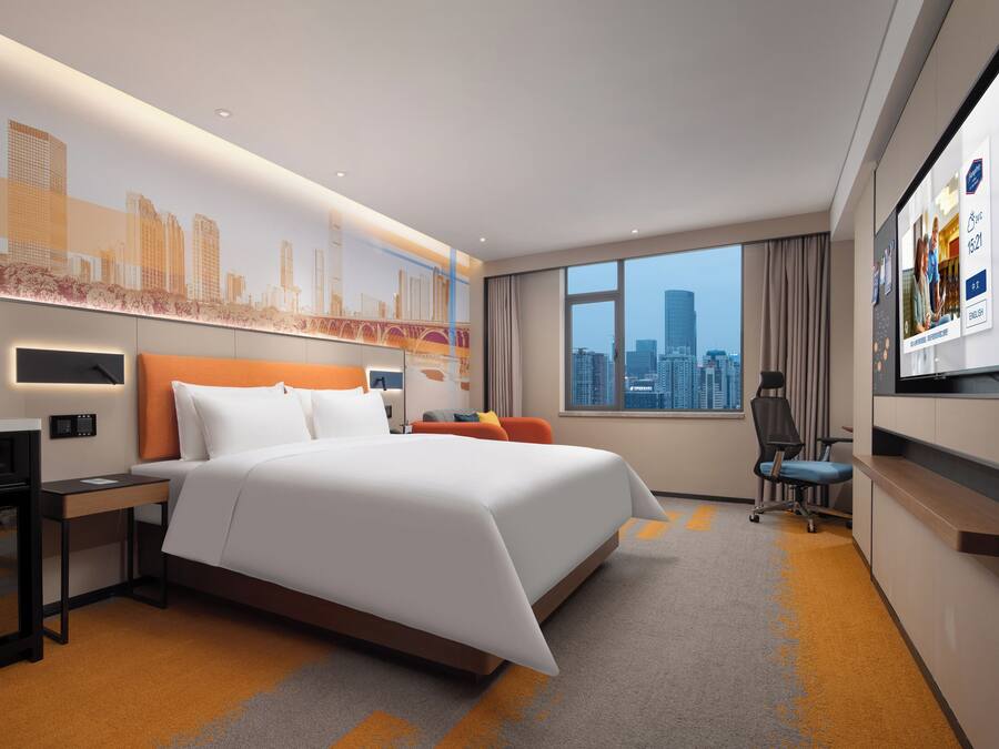 Habitación de hotel moderna con una cama grande, un escritorio, una silla y vistas a la ciudad.