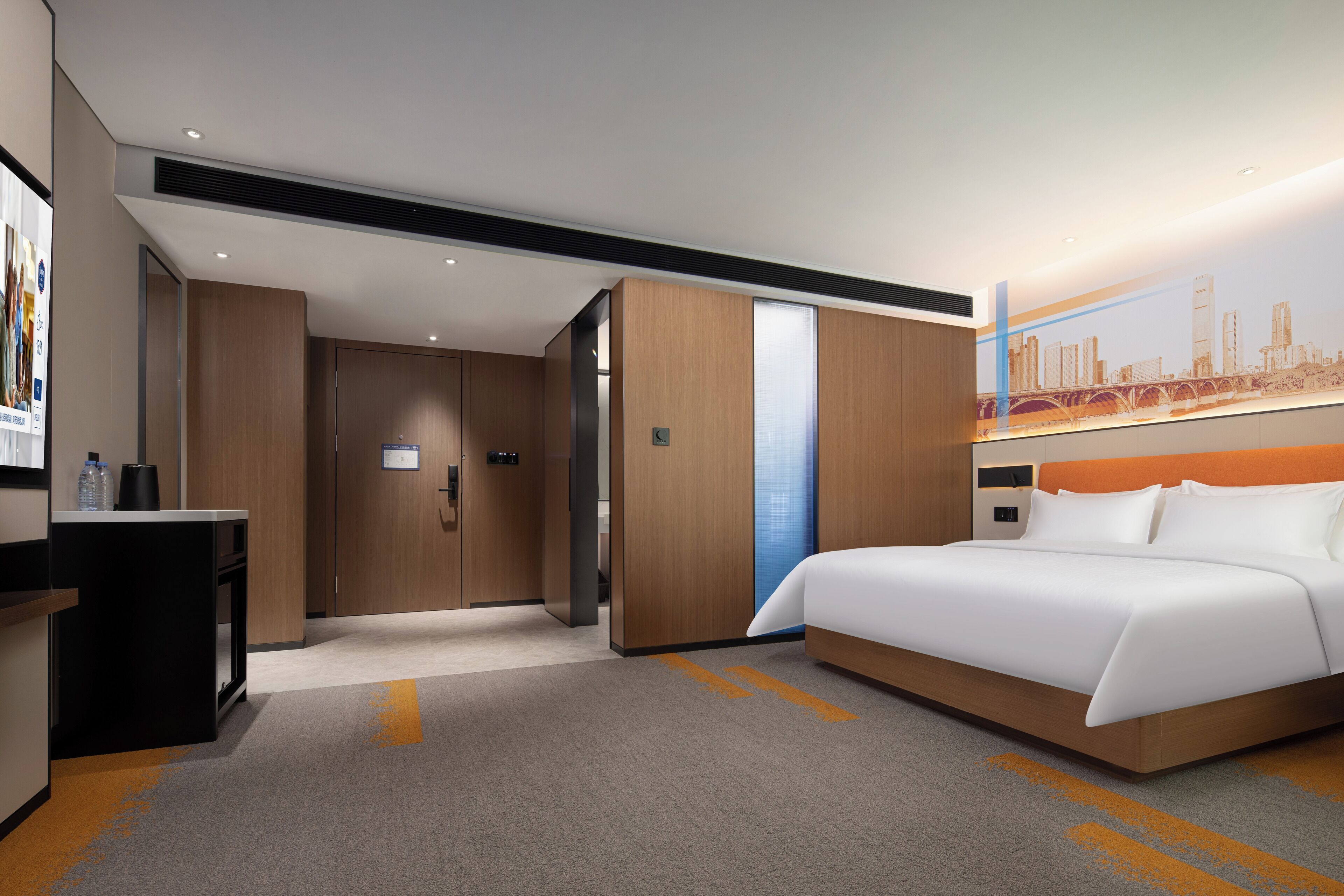 Una habitación de hotel moderna con una cama grande, un escritorio con una computadora y un mural con vistas a la ciudad en la pared.