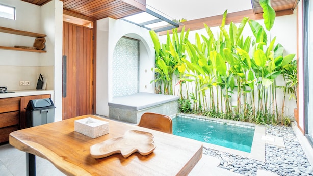 Ein moderner Poolbereich im Freien mit einem Holztisch, Stühlen und einem kleinen Pool, umgeben von tropischen Pflanzen.