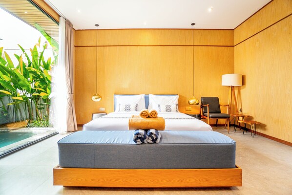 A modern bedroom with a large bed, a bedside table, a chair, a lamp, and a view of a pool.