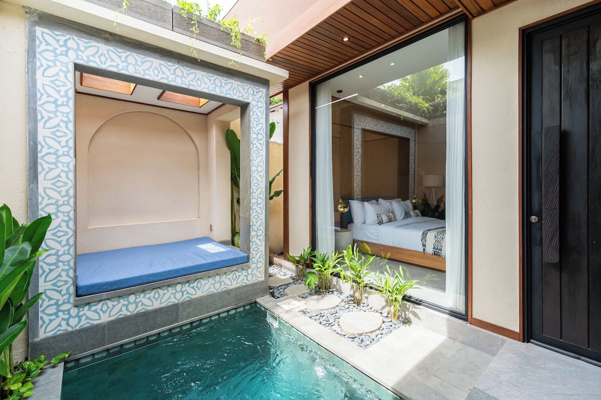 A modern bathroom with a built-in bench, a small pool, and a view into a bedroom with a bed and a nightstand.