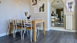 A dining area with a wooden table and white chairs, a vase with dried flowers, and three hanging pendant lights.