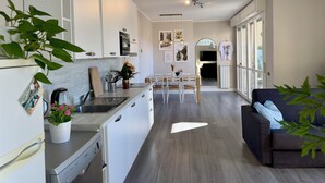 A modern kitchen with white cabinets, a dining area with a table and chairs, and a sofa in the living area.