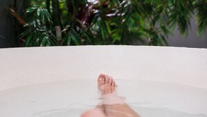 A bathtub with a person's feet in it, surrounded by green plants.