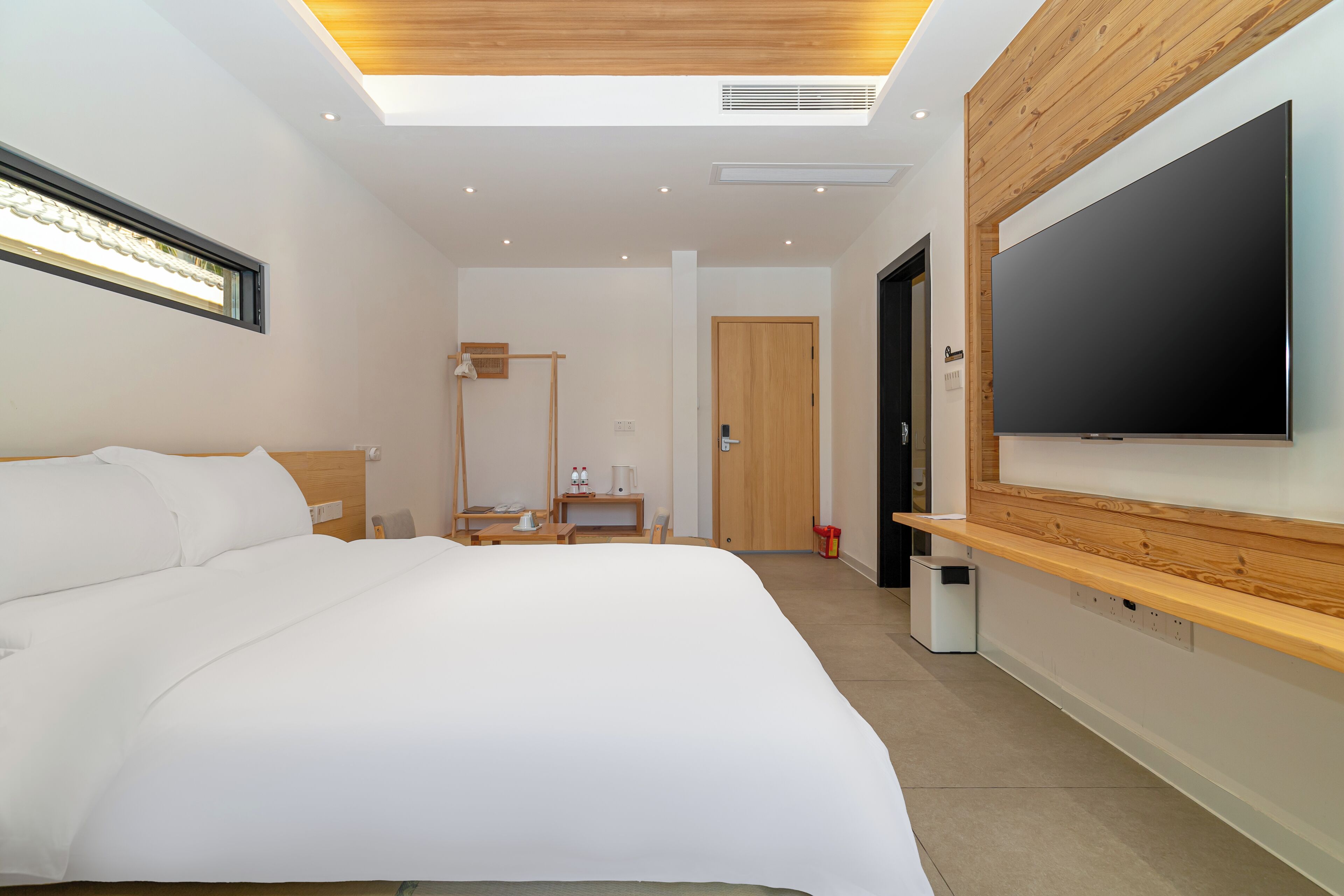 Quarto de hotel moderno com uma cama grande, televisão de tela plana na parede, escrivaninha com luminária e um closet espaçoso.