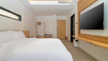 Quarto de hotel moderno com uma cama grande, televisão de tela plana na parede, escrivaninha com luminária e um closet espaçoso.