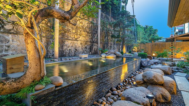 Ein friedlicher Garten mit einer Steinmauer, einer hölzernen Bank und einem Wasserspiel.