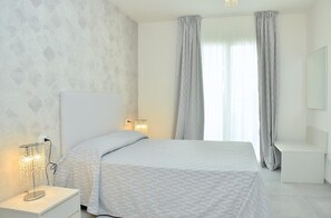 A modern bedroom with a large bed, two bedside lamps, a nightstand, and a dresser.