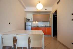 A compact kitchen with a dining area, featuring a white table and chairs, a microwave, a refrigerator, and orange cabinets. - Sea view apartment in the heart of Bibione (Bibione)