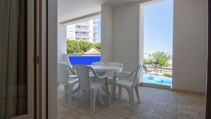 Un balcón con mesa y sillas, vista a una piscina y un edificio al fondo.