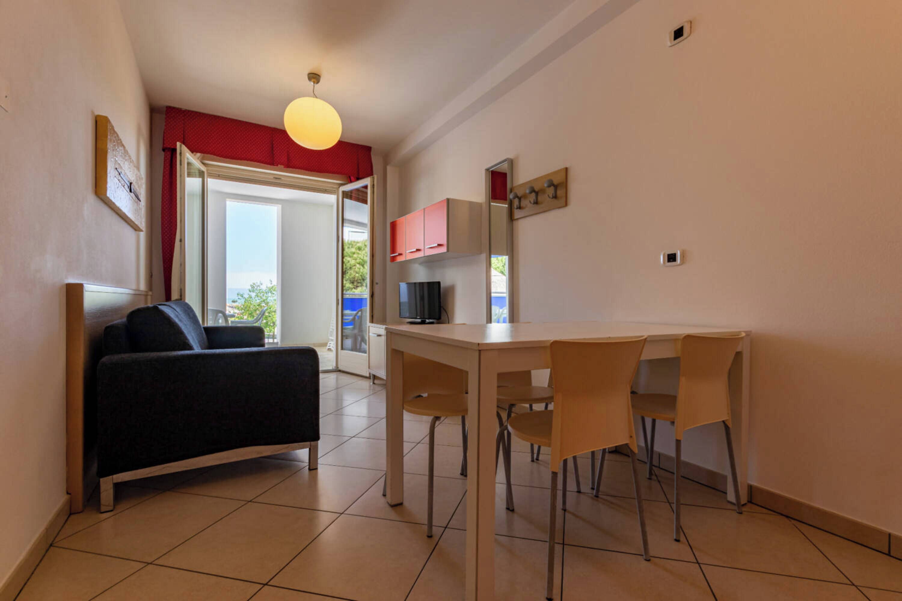 Un espace de vie compact comprenant un canapé, une table à manger avec des chaises, un téléviseur et une fenêtre à cadre rouge.
