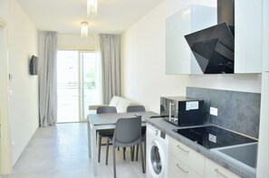 Una cocina moderna con microondas, estufa y lavadora integrados. Cuenta con una zona de comedor con mesa y sillas, y un ventanal con cortinas.