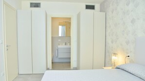 Ein Schlafzimmer mit Bett, Nachttisch, Nachttischlampe und einem durchgegangenen Tür sichtbaren Badezimmer.