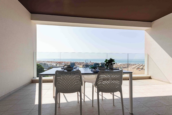 A balcony with a table and two chairs, overlooking a beach and cityscape.