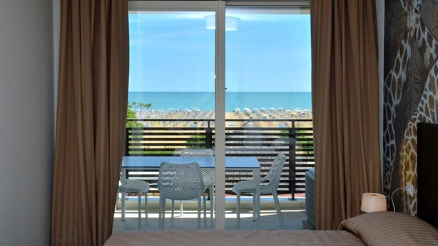 Ein Hotelzimmer mit einer großen Schiebeglasdoor, die auf einen Balkon mit Blick auf Strand und Meer führt.