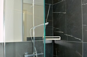 Ein modernes Badezimmer mit einer Duschkabine aus Glas, einer Wand aus schwarzem Marmor und einer sichtbaren Bedienblende für die Dusche.