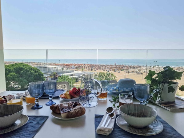 A breakfast setup with a view of a crowded beach and ocean.
