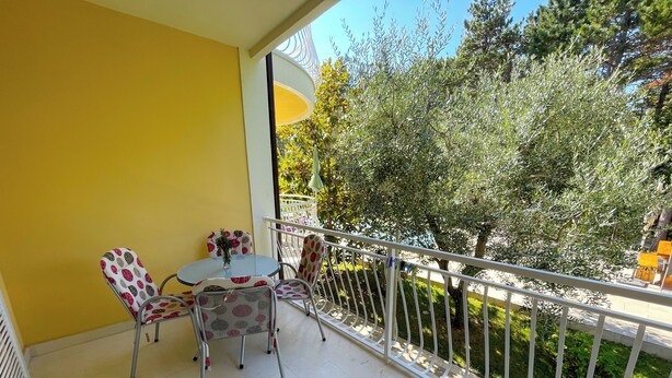 Un balcón con una pared amarilla, una mesa con sillas y vistas a árboles y follaje.
