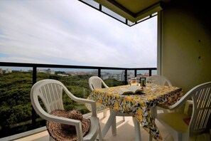 Un balcon avec une table et des chaises, offrant une vue sur le paysage urbain et la verdure.