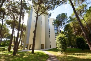 Un bâtiment moderne avec une entrée centrale, entouré d’une pelouse bien entretenue et de grands arbres.