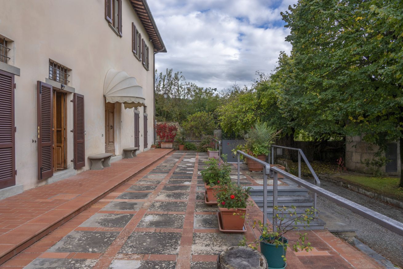 Ein Innenhof mit einem gefliesten Weg, Blumentöpfen, einer Treppe und einem Gebäude mit Fensterläden.