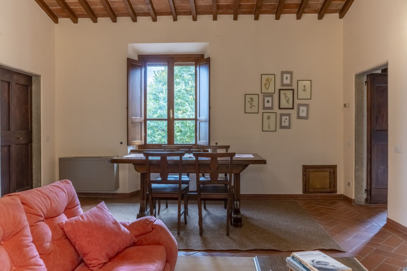 Ein gemütliches Zimmer mit Esstisch, Stühlen, einer Couch und einem Fenster mit Blick auf Grünflächen.