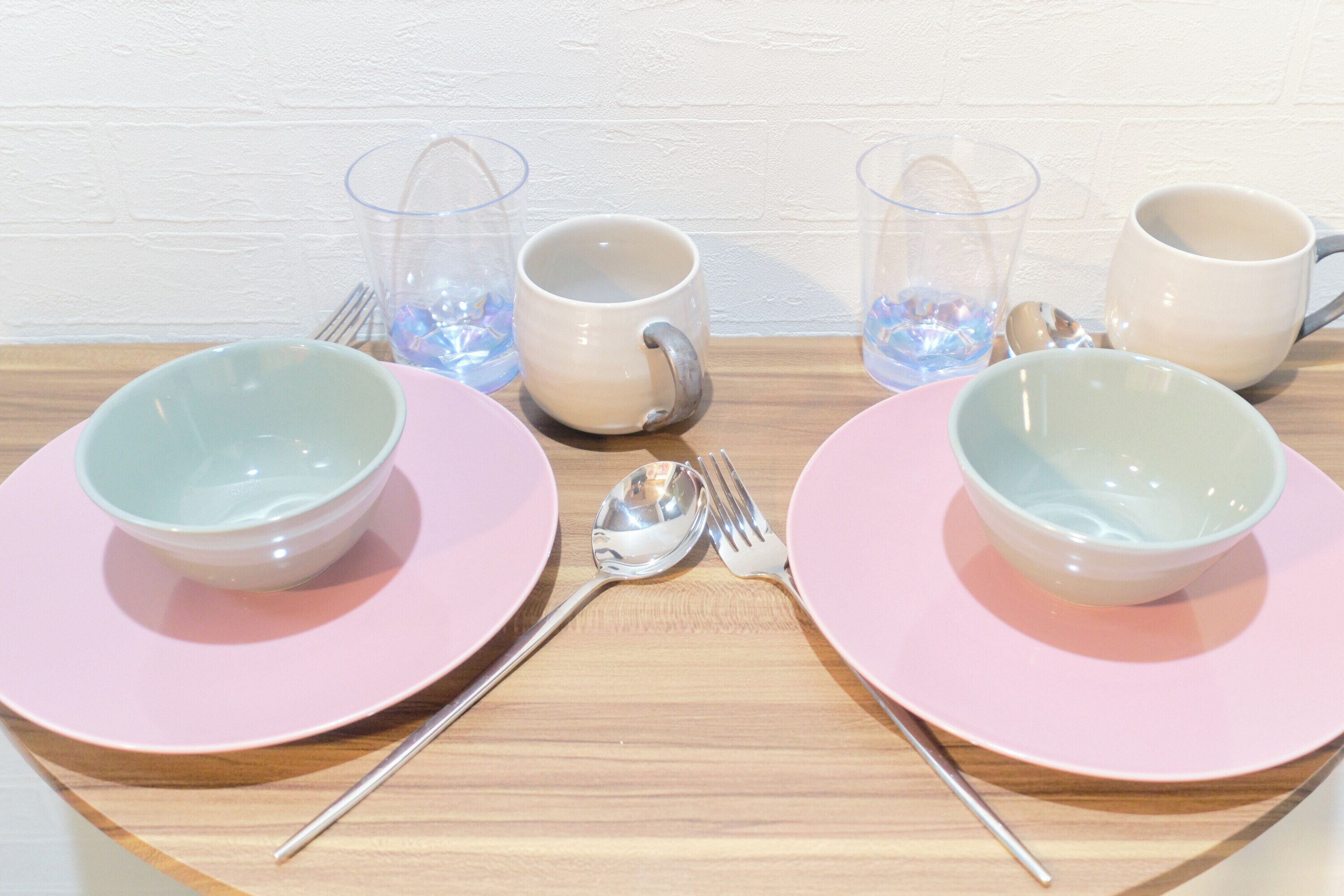 Una mesa servida con platos rosas, vasos transparentes y tazas blancas.