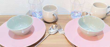 Una mesa servida con platos rosas, vasos transparentes y tazas blancas.
