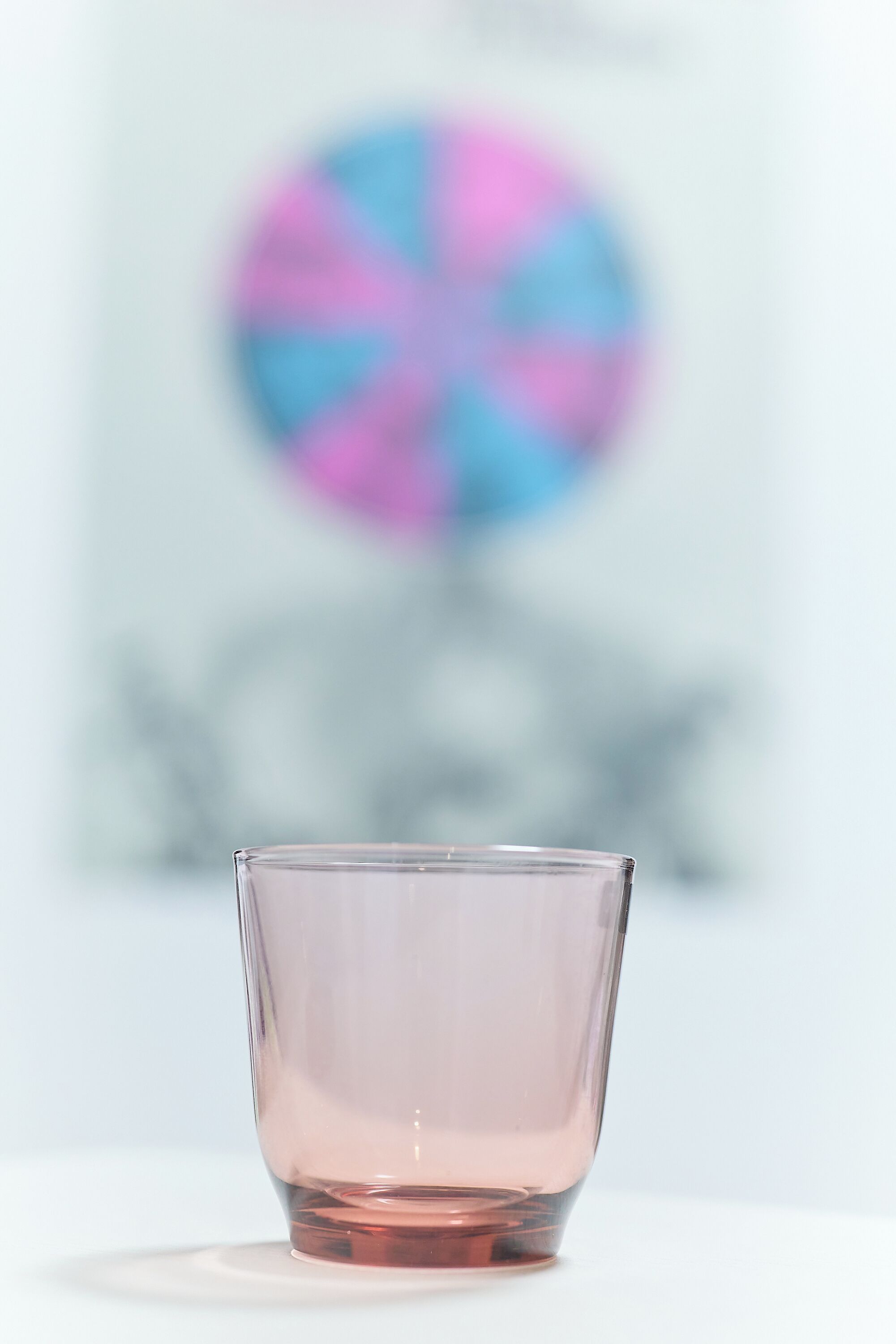 A clear glass with a pink tint, a white surface, and a blurred background with a circular pattern.
