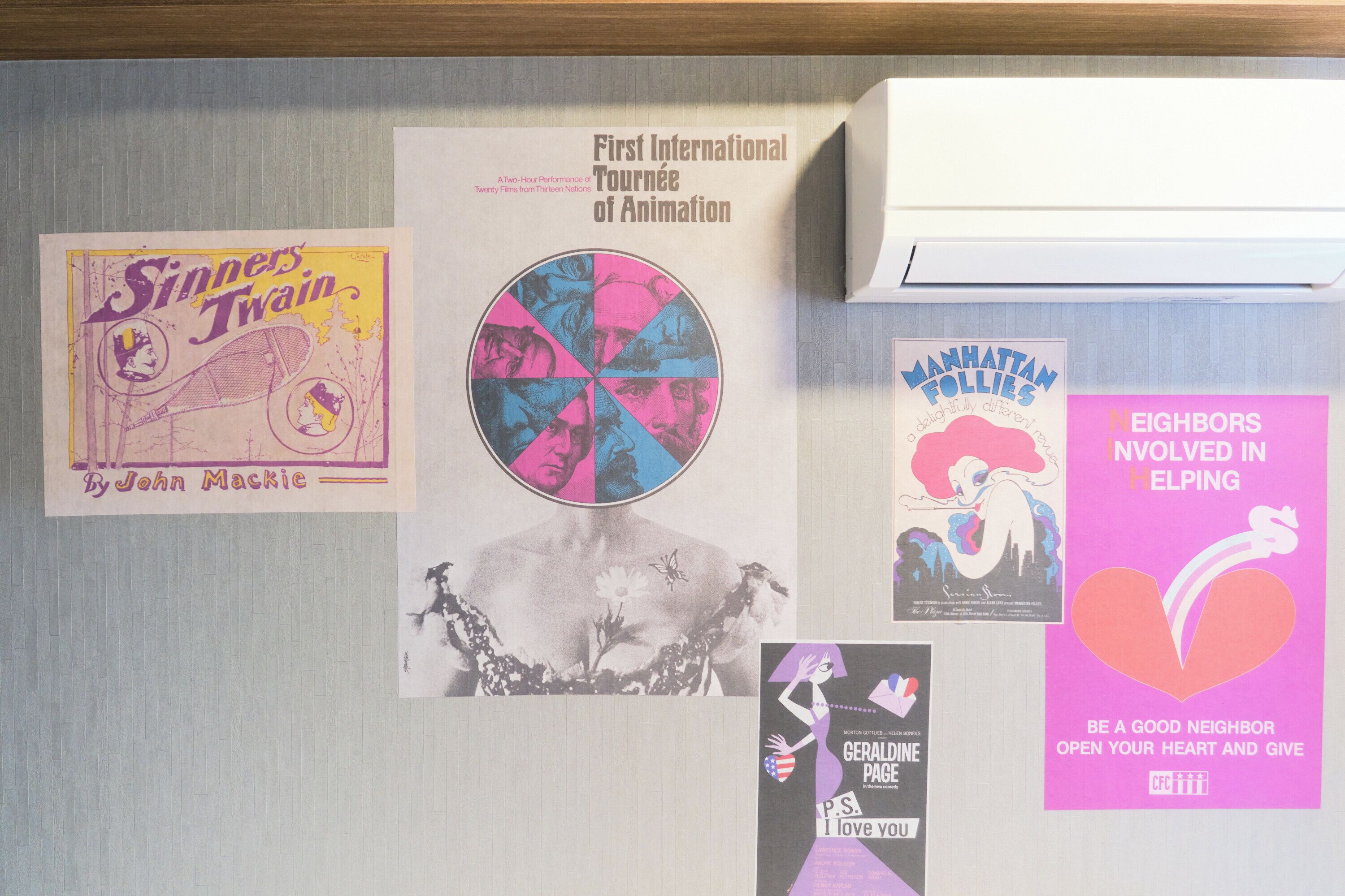 En opslagstavle med forskellige plakater og foldere, heriblandt en om den første internationale Animations Tournée og en anden der opfordrer naboer til at hjælpe hinanden.