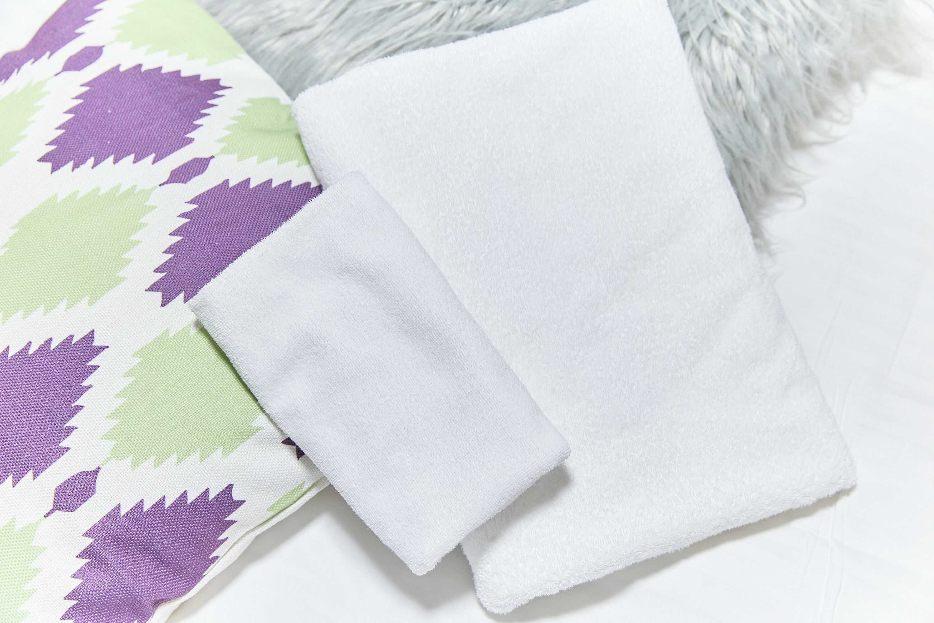 Toalha branca e almofada estampada com desenhos de folhas verdes e roxas.
