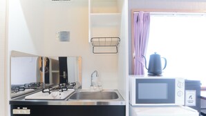 A compact kitchen with a stainless steel sink, a microwave, and a kettle on the counter. - Marine Cove Hatsudai by Tranova (Tokyo)