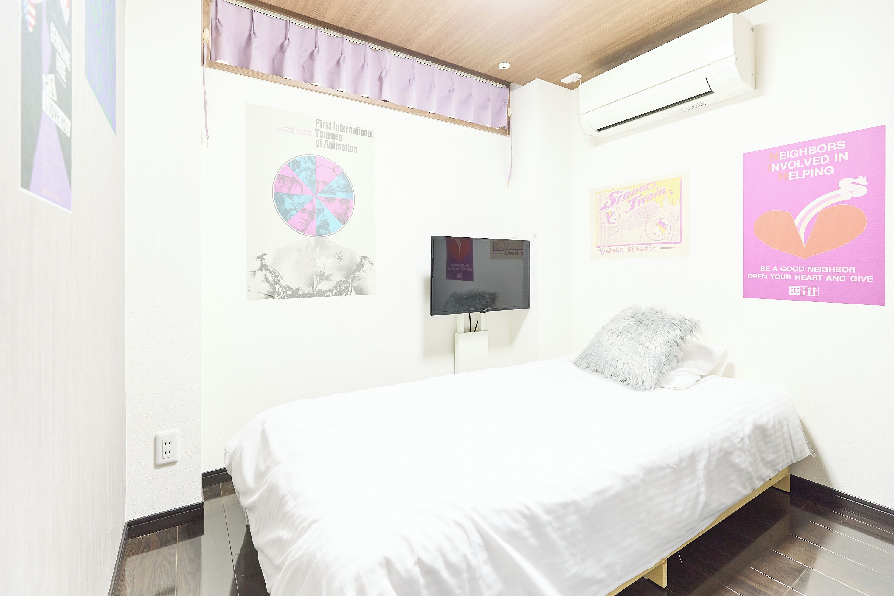 A bedroom with a bed, a television, and various posters on the wall.