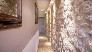 A hallway with stone walls and a tiled floor, leading to a door at the end. - Le Marais Sicile (Paris)
